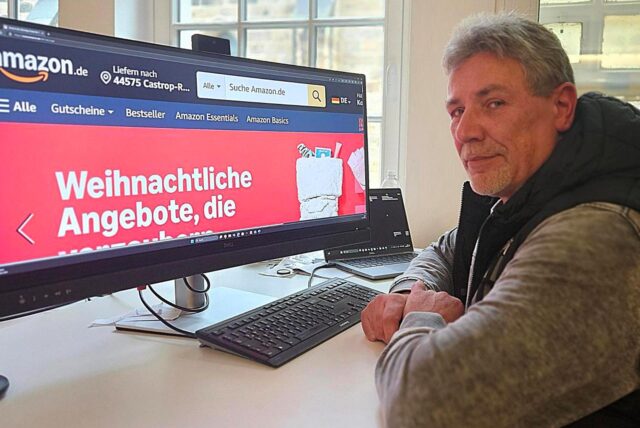 Mann sitzt vor einem Computerbildschirm, auf dem die Startseite von Amazon zu sehen ist