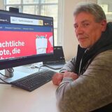 Mann sitzt vor einem Computerbildschirm, auf dem die Startseite von Amazon zu sehen ist