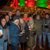Eine Gruppe Menschen mit Glühwein vor dem beleuchteten Rathaus