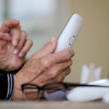 Eine ältere Person hält ein Telefon in den Händen.