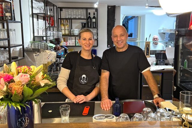 Ex-BVB-Spieler Giuseppe „Billy“ Reina und seine Frau Julia haben das Bistro SiSi auf der Massener Str. 21 in Unna eröffnet. Die beiden neuen Inhaber stehen gemeinsam hinter der Theke neben einem Blumenstrauß und lächeln.