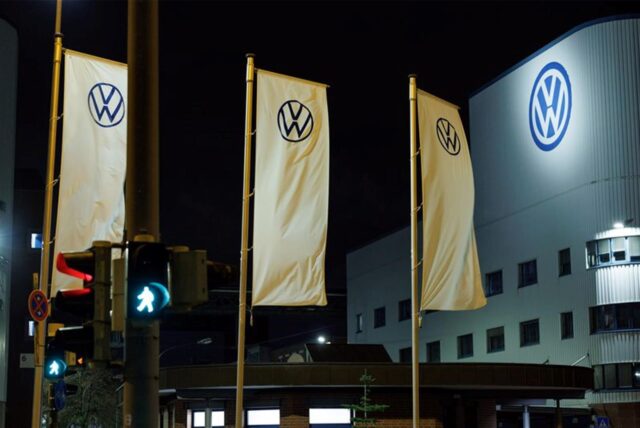 Mehrere wehende Fahnen mit dem VW-Logo vor einem Gebäude mit dem VW-Logo.