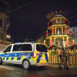 Bei Nacht steht ein Polizeiwagen vor einem dekorativen Turm des Dortmunder Weihnachtsmarktes. Zwei Passanten gehen vorbei.