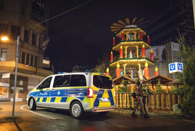 Bei Nacht steht ein Polizeiwagen vor einem dekorativen Turm des Dortmunder Weihnachtsmarktes. Zwei Passanten gehen vorbei.