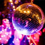 Im Vordergrund eine schimmernde Disco-Kugel, im Hintergrund tanzende Menschen