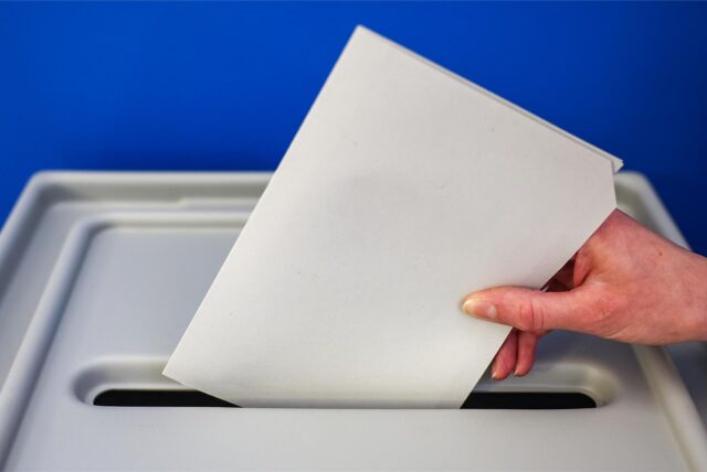 Ein Stimmzettel wird in eine Wahlurne geworfen.