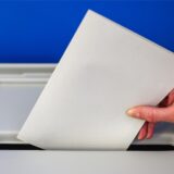 Ein Stimmzettel wird in eine Wahlurne geworfen.