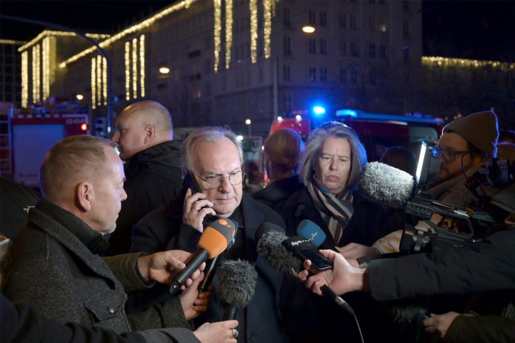 Ministerpräsident Reiner Haseloff, umringt von Reportern, viele Mikrofone, im Hintergrund Blaulicht und Einsatzfahrzeuge. Ministerpräsident Reiner Haseloff, umringt von Reportern, viele Mikrofone, im Hintergrund Blaulicht und Einsatzfahrzeuge.