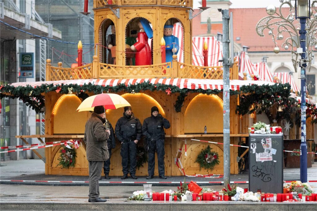 Ein Passant mit Regenschirm und Polizisten stehen vor dem Weihnachtsmarkt. Ein Passant mit Regenschirm und Polizisten stehen vor dem Weihnachtsmarkt.