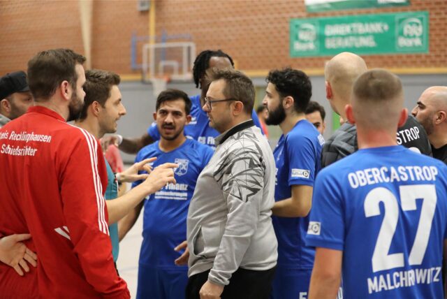 Bei einem Fußball-Hallenturnier versammelt sich eine Traube aus Spielern und Offiziellen um den Schiedsrichter.