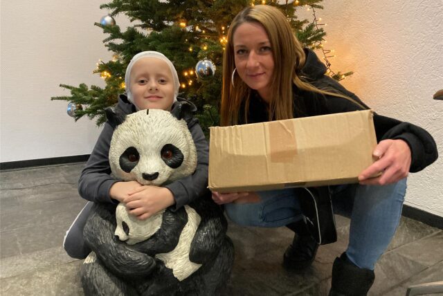 Conner aus Marl und seine Mutter hocken vor einem Weihnachtsbaum und halten Geschenke aus einer Spendenaktion in den Händen.