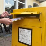 Ein Mann wirft Briefe in einen gelben Briefkasten