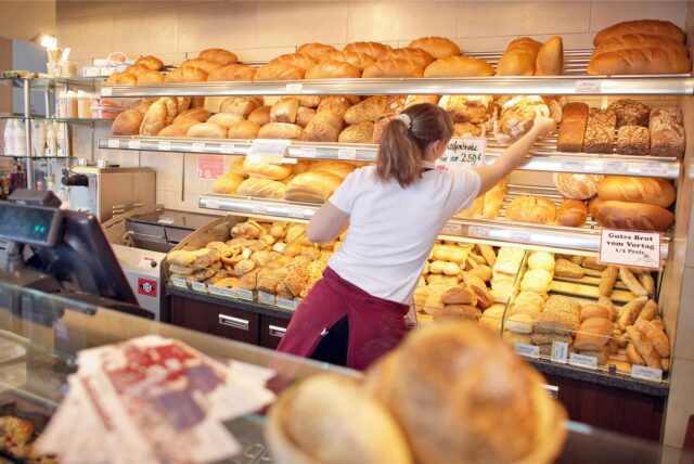 Eine Bäckereifachverkäuferin greift nach einem Brot im Regal (Symbolbild).