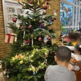 Kinder stehen vor einem geschmückten Weihnachtsbaum.