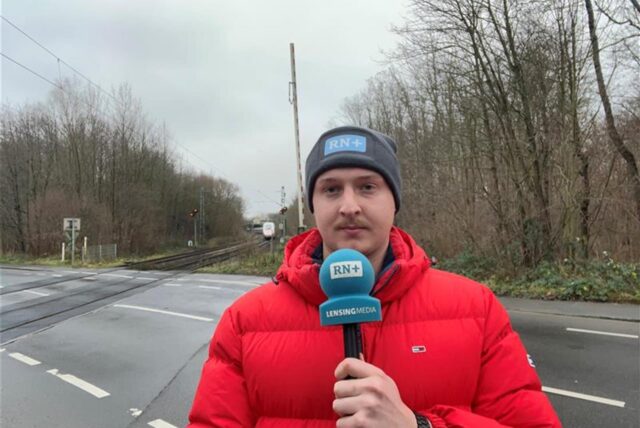 Ein Reporter steht mit einem Mikrofon in der Hand an einem Bahngleis in Dortmund-Kirchderne.