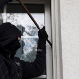 Ein Einbrecher hebelt eine Tür mit einer Brechstange auf.
