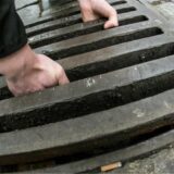 Zwei Männerhände greifen in einen Gullydeckel und sind im Begriff, diesen aus einem Schacht zu heben. (Symbolbild)