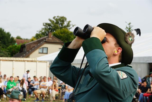 Ein Schütze beobachtet mit einem Fernglas das Vogelschießen des Bürger- und Schützenvereins Oberwiese.