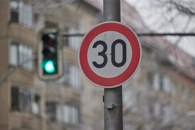 Ein Tempo-30-Schild an einer Kreuzung, im Hintergrund eine grüne Ampel