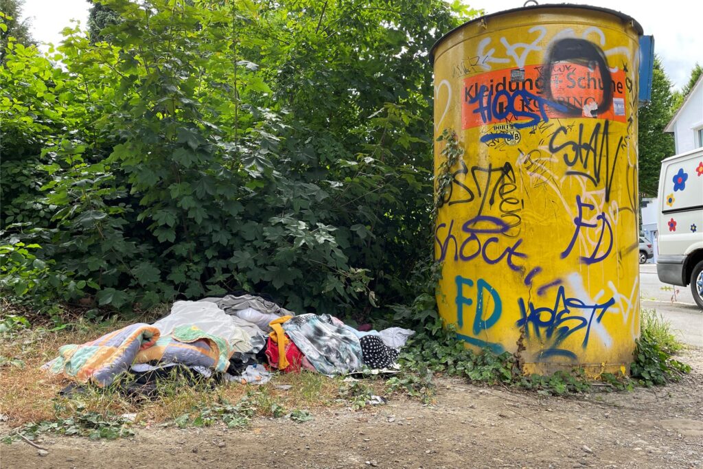 Textilien liegen neben einem Altkleidercontainer. Textilien liegen neben einem Altkleidercontainer.