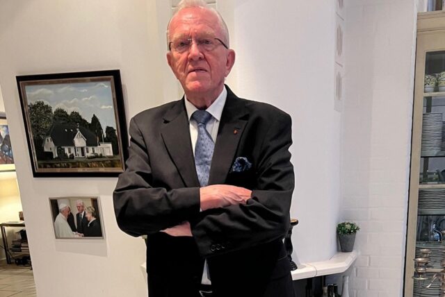 Hubert Schulte-Kemper steht mit verschränkten Armen, klassisch gekleidet im schwarzen Anzug, weißes Hemd, hellblaue Krawatte, in seinem Haus in Alt-Marl.