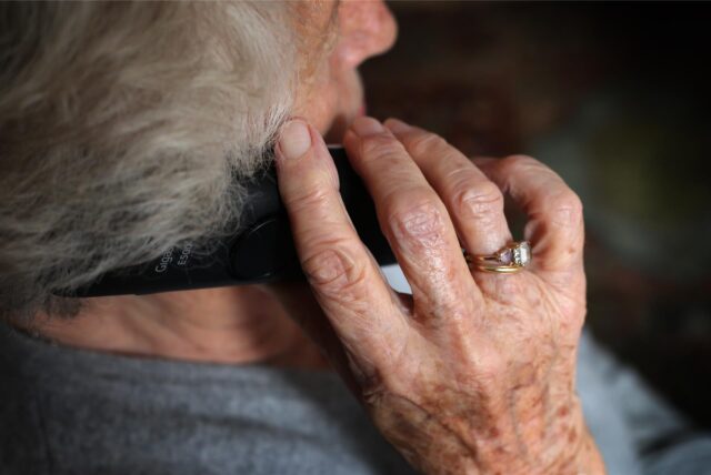 Eine Seniorin mit weißem Haar und grauem Pullover beim Telefonieren, von hinten fotografiert. (Symbolfoto)
