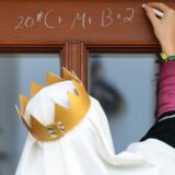 Ein Sternsinger schreibt an Heilige Drei Könige mit Kreide den Segenspruch „C+M+B“ an eine Haustür.