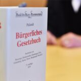 An der Richterbank eines Sitzungssaals beim Oberlandesgericht (OLG) sitzt ein Richter mit Richterrobe, davor steht ein Bürgerliches Gesetzbuch