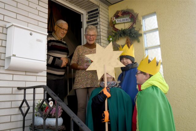 Drei Sternsinger stehen in Herten-Süd vor einer Haustür. Im Eingang steht ein älteres Ehepaar.