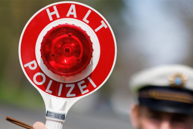 Ein Beamter hält eine Kelle mit der Aufschrift „Halt Polizei“ hoch.