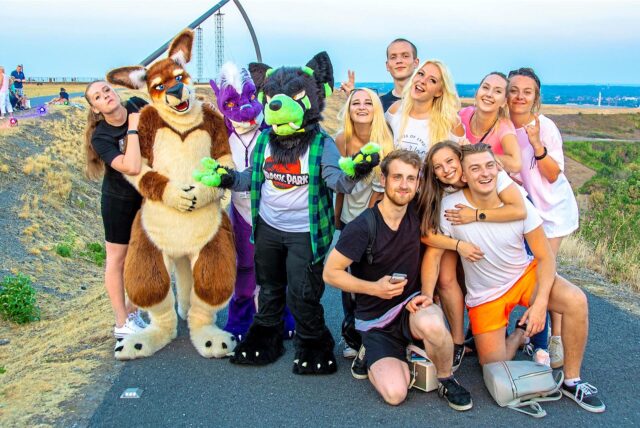 Auf dem Plateau der Halde Hoheward in Herten-Süd hat sich eine Besuchergruppe des Haldenglühens zum Gruppenfoto aufgestellt. Drei Personen sind in einem Kostüm.