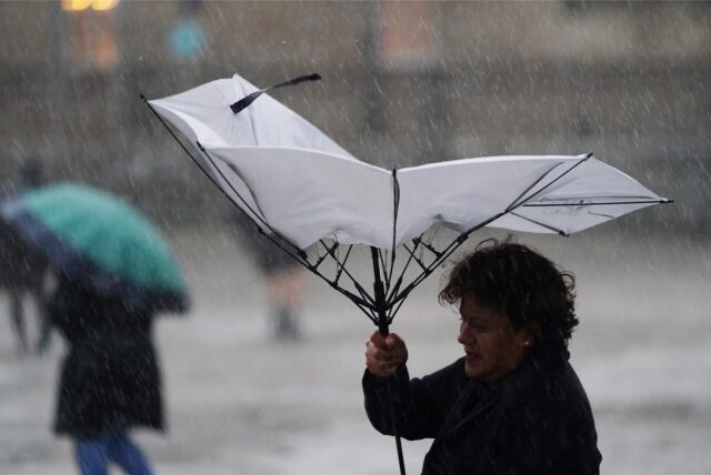 Eine Frau kämpft bei Sturm mit ihrem Regenschirm.