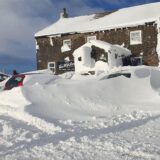 Vor einem alten Backsteingebäude liegen Massen an Schnee. Auch die Autos auf dem Vorhof sind eingeschneit.