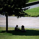 Zwei Personen sitzen im Schatten uuchen den Schatten unter einem Baum.