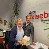 Simone Brenner und Christoph Klix stehen in einem Reisebüro