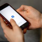 Eine Person hält ein Smartphone in den Händen, auf dem das Facebook-Logo – ein weißes „F“ auf blauem Grund – angezeigt wird.