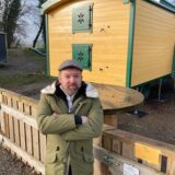 Dennis Alexander Lauer steht mit verschränkten Armen vor den gelben Bauwagen des Vereins Cum Natura in Herten-Scherlebeck.