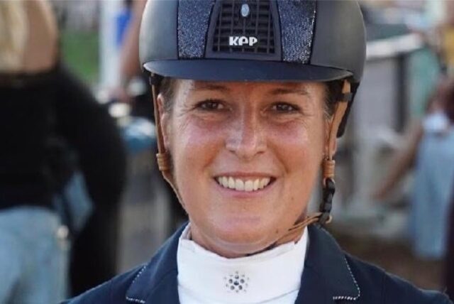 Kristina Kerlen auf dem Reitplatz in Reiterjoppe und mit Schutzhelm.