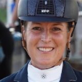 Kristina Kerlen auf dem Reitplatz in Reiterjoppe und mit Schutzhelm.