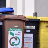 Mehrere Mülltonnen stehen nebeneinander vor einem Haus.