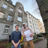Nathaniel Pangan und Lars Urban stehen vor der gräulichen Fassade ihres bisherigen Wohnhauses, Urban hält das Kündigungsschreiben des Vermieters in die Kamera.