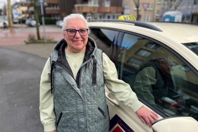 Brigitte Meer steht neben einem Taxi.