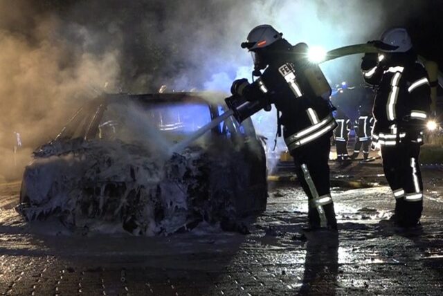 Zwei Feuerwehrleute mit Atemschutzmasken löschen einen Pkw.