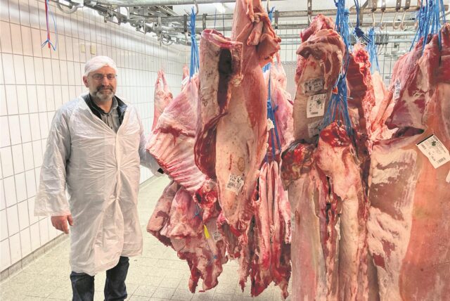 Ein Mann zeigt Fleischhälften in einem Kühlhaus.
