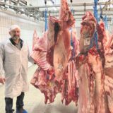 Ein Mann zeigt Fleischhälften in einem Kühlhaus.