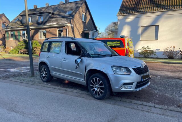 Ein grauer Skoda mit beschädigter Seite steht am Straßenrand, im Hintergrund ein Einsatzfahrzeug mit der Aufschrift „Rettungsdienst“.