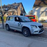 Ein grauer Skoda mit beschädigter Seite steht am Straßenrand, im Hintergrund ein Einsatzfahrzeug mit der Aufschrift „Rettungsdienst“.