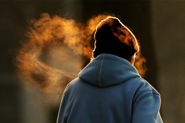 Man sieht eine Frau von hinten, sie trägt eine warme, blaue Jacke und eine dunkle Mütze. Über ihrem Kopf schwebt Atemkondensat in der Luft.