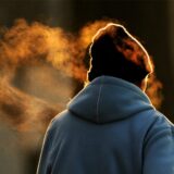 Man sieht eine Frau von hinten, sie trägt eine warme, blaue Jacke und eine dunkle Mütze. Über ihrem Kopf schwebt Atemkondensat in der Luft.