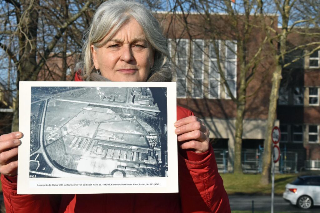 Die Historikerin hält eine Luftbildaufnahme des Geländes von 1942/43 in den Händen. Die Baracken sind deutlich zu erkennen. Die Historikerin hält eine Luftbildaufnahme des Geländes von 1942/43 in den Händen. Die Baracken sind deutlich zu erkennen.